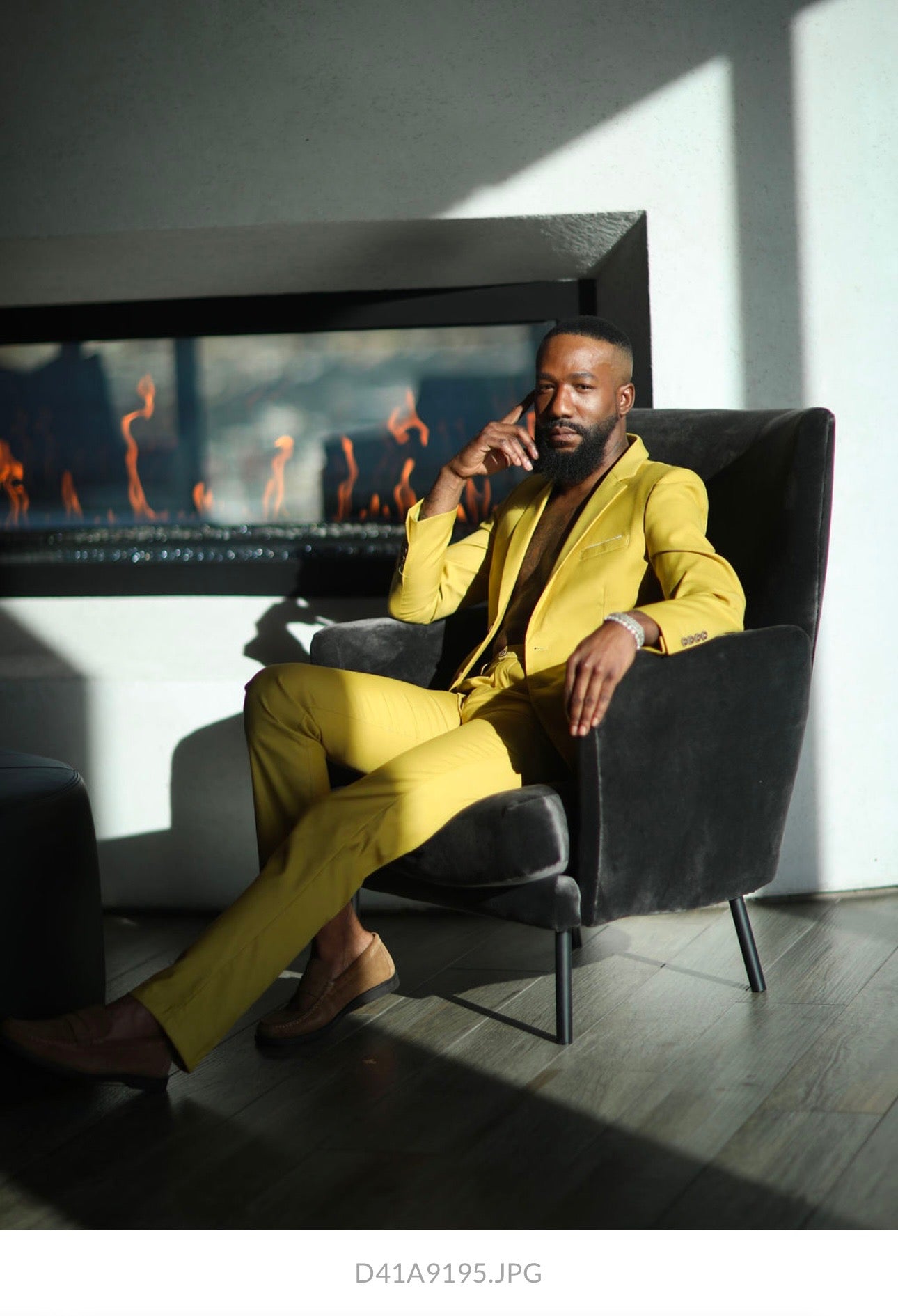 Dior Sovoa in a yellow suit sitting in front of a fireplace