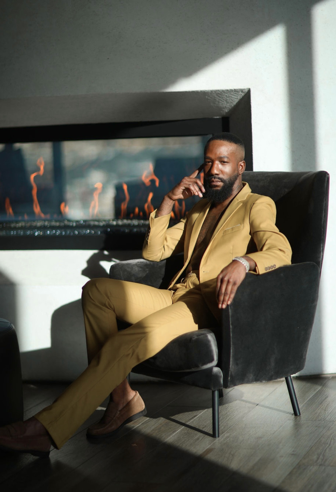 Dior Sovoa in a yellow suit sitting in front of a modern fireplace
